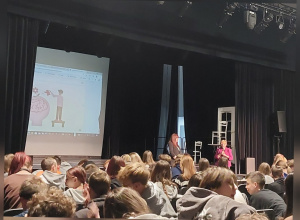 Uczniów z widowni oglądają dwie osoby prowadzące edukacyjny spektakl.