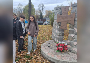 Uczniowie stoją pod pomnikiem upamiętniającym żołnierzy wyklętych.