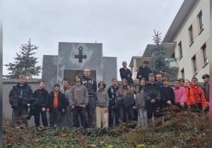 Uczniowie stoją pod pomnikiem upamiętniającym żołnierzy podziemia.