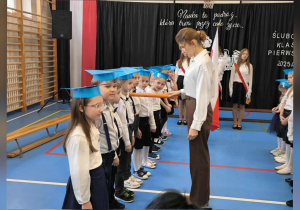 Pani Dyrektor dokonuje symbolicznego aktu pasowania pierwszoklasistów, dotykając ich ramienia dużym ołówkiem.