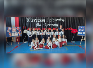 Uczniowie klasy III b wspólnie z wychowawczynią stoją przed dekoracją nawiązującą do Narodowego Święta Niepodległości.