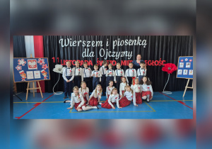 Uczniowie klasy III b wspólnie z wychowawczynią stoją przed dekoracją nawiązującą do Narodowego Święta Niepodległości.