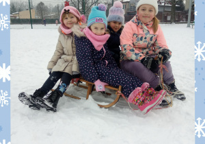 Dziewczynki siedzą na sankach, otoczone białym, puszystym śniegiem.