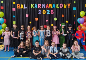 Dzieci w kolorowych przebraniach pozujących przed dekoracją z napisem „Bal Karnawałowy 2026” i motywem LEGO.