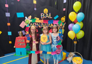 Dzieci w kolorowych przebraniach pozujących przed dekoracją z napisem „Bal Karnawałowy 2026”.