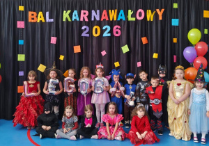 Dzieci w kolorowych przebraniach pozujących przed dekoracją z napisem „Bal Karnawałowy 2026” i motywem LEGO.