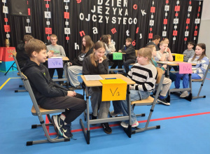 uczniowie siedzą w grupach przy stolikach i biorą udział w obchodach Dnia Języka Ojczystego.
