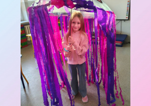 Dziewczynka stoi pod kolorową parasolką.