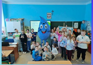 Uczniowie stoją obok dużej, niebieskiej maskotki w kształcie kropli wody. Światowy Dzień Wody