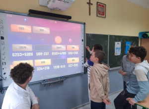 Uczniowie na ekranie multimedialnym wykonują zadania matematyczne.