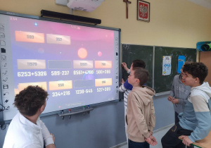 Uczniowie na ekranie multimedialnym wykonują zadania matematyczne.