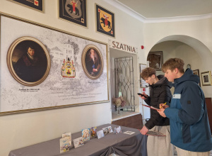 Uczniowie oglądają muzealną tablicę z portretami i informacjami o rodzinie Ostrowskich.