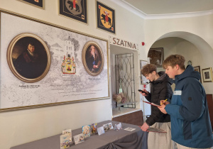 Uczniowie oglądają muzealną tablicę z portretami i informacjami o rodzinie Ostrowskich.