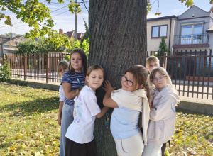 Dziewczynki z klasy III a przytulają się do drzewa.
