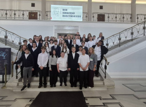 Na zdjęciu widoczna jest grupa uczniów wraz z opiekunami podczas wizyty edukacyjnej w gmachu Sejmu Rzeczypospolitej Polskiej. Uczestnicy pozują do wspólnego zdjęcia na reprezentacyjnych scho