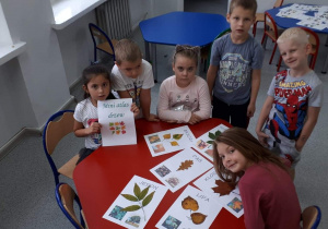 Na fotografii znajduje się sześcioro dzieci, które wspólnie przy stoliku tworzą atlas drzew do kącika przyrody.