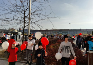 Uczniowie z białymi i czerwonymi balonami przed rozgrzewką do biegu