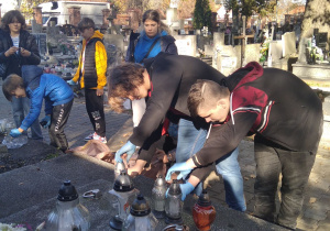 Uczniowie zapalają znicze na grobie